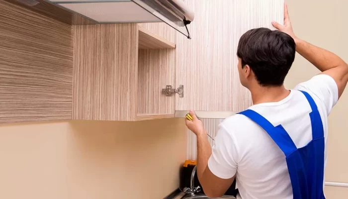 a man in a blue overalls measuring a shelf